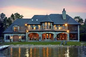 French country stone lake house with covered verandas and stone turret.